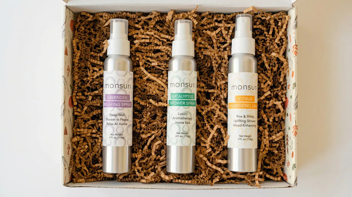 Overhead view of the open Monsuri kraft gift box on shredded kraft fill with the lavender, eucalyptus and citrus 4 oz sprays side by side