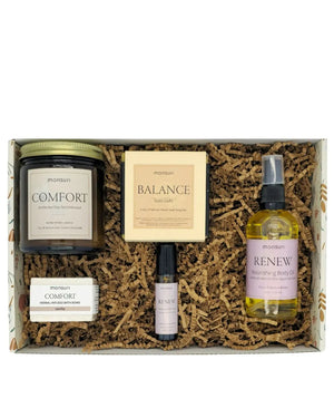 The Birthday Bliss set open in the Monsuri kraft gift box on shredded kraft fill - the COMFORT candle, the BALANCE Gobi Gold soap, the vanilla bath bomb, the Floral Radiance roller and the RENEW body oil