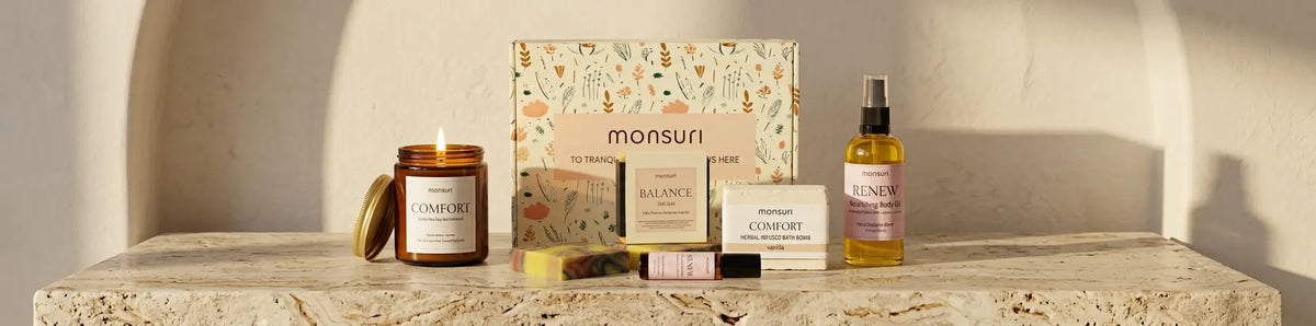 The Birthday Bliss set along a travertine ledge in an arched alcove, the candle lit beside the gift box, the soap, the bath bomb, the roller and the body oil