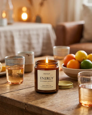 Monsuri ENERGY citrus grapefruit candle glowing on a rustic wood table at dusk, next to citrus drinks and a bowl of whole citrus fruit.