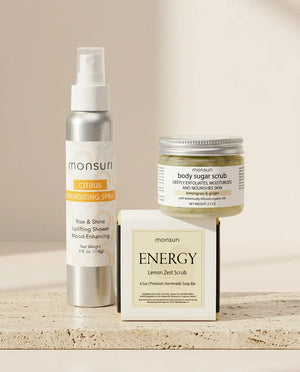 All three pieces on a travertine ledge - the 4 oz CITRUS energizing spray, the 2.5 oz lemongrass and ginger body sugar scrub and the ENERGY lemon zest scrub soap bar