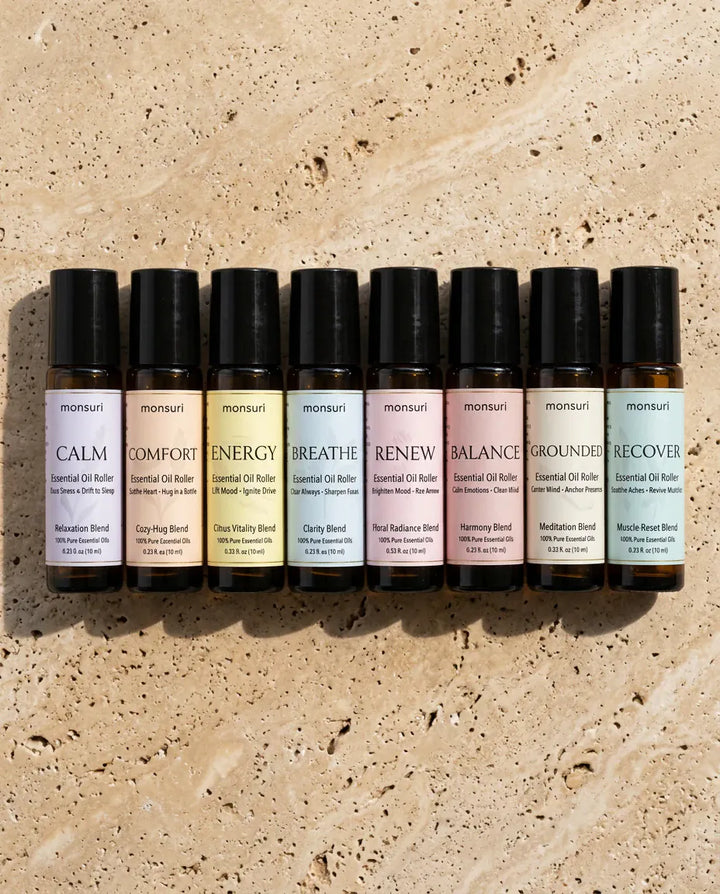 The eight Monsuri essential oil rollers laid out on travertine, each labelled with its blend and 0.33 fl oz (10 ml)