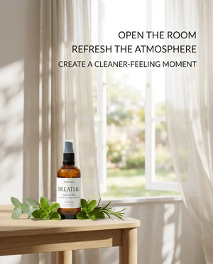 Monsuri BREATHE eucalyptus hydrosol on a wood table by an open window with sheer curtains, captioned open the room, refresh the atmosphere.