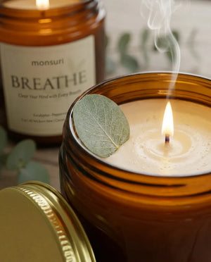 Close-up of the Monsuri BREATHE candle's cotton wick and even wax pool burning, with a eucalyptus leaf resting on the melted wax.