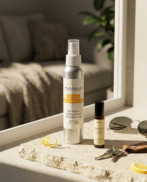 The 4 oz citrus energizing shower spray and the ENERGY essential oil roller on a sunlit windowsill beside a set of keys and sunglasses