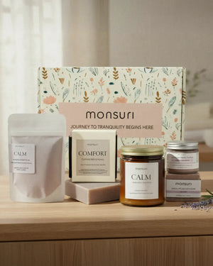Mom's Wind-Down Ritual in front of its botanical kraft gift box: the lavender bath soak pouch, the oatmeal milk and honey soap, the CALM lavender chamomile candle, the lavender whipped body butter and the lavender bath bomb, with dried lavender on a wooden surface.