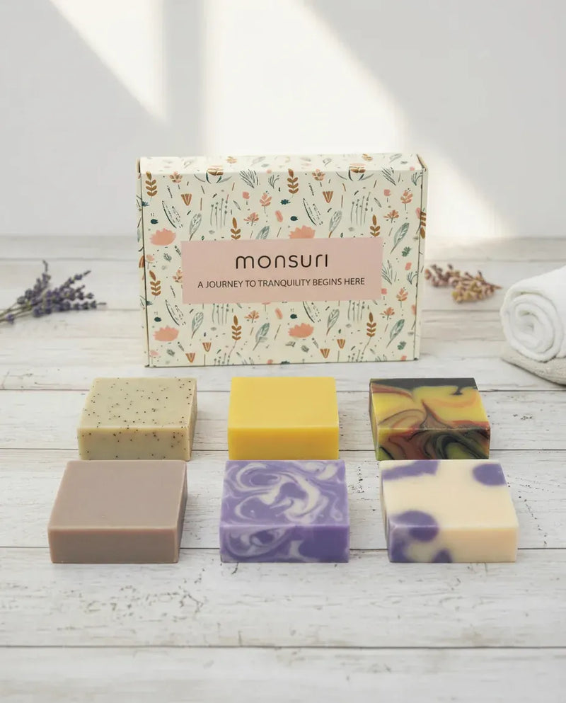 Monsuri Rest & Renewal soap gift set — six full-size handmade bars and the botanical gift box laid out on white wood.