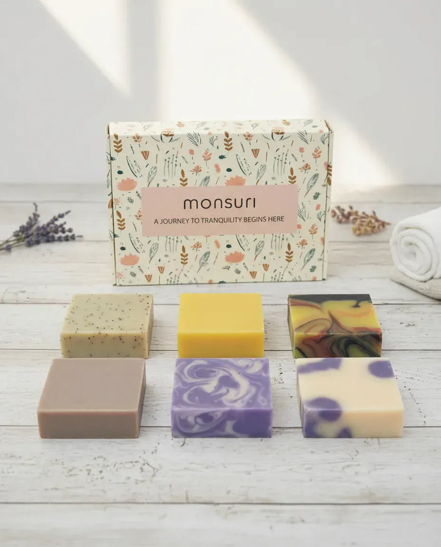 Monsuri Rest & Renewal soap gift set — six full-size handmade bars and the botanical gift box laid out on white wood.