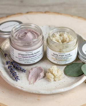 A hand reaching for the Monsuri whipped body butter jar with the three Sensory Symphony shower sprays lined up behind it.