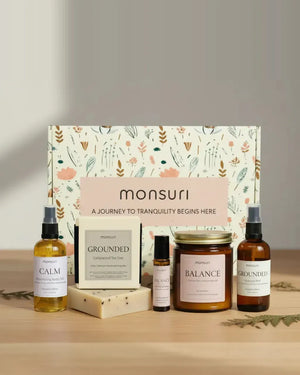 Stress-Less Sanctuary five-piece set in front of the Monsuri botanical gift box - CALM nourishing body oil 3.3 fl oz, GROUNDED cedarwood and tea tree soap 4.5 oz, BALANCE essential oil roller, BALANCE palo santo candle 7 oz with a 45 hour burn, and GROUNDED hydrosol mist 3.3 fl oz