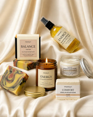 The five pieces gathered on cream silk with the ENERGY candle lit, its gold lid set down beside the marbled Gobi Gold soap bar.