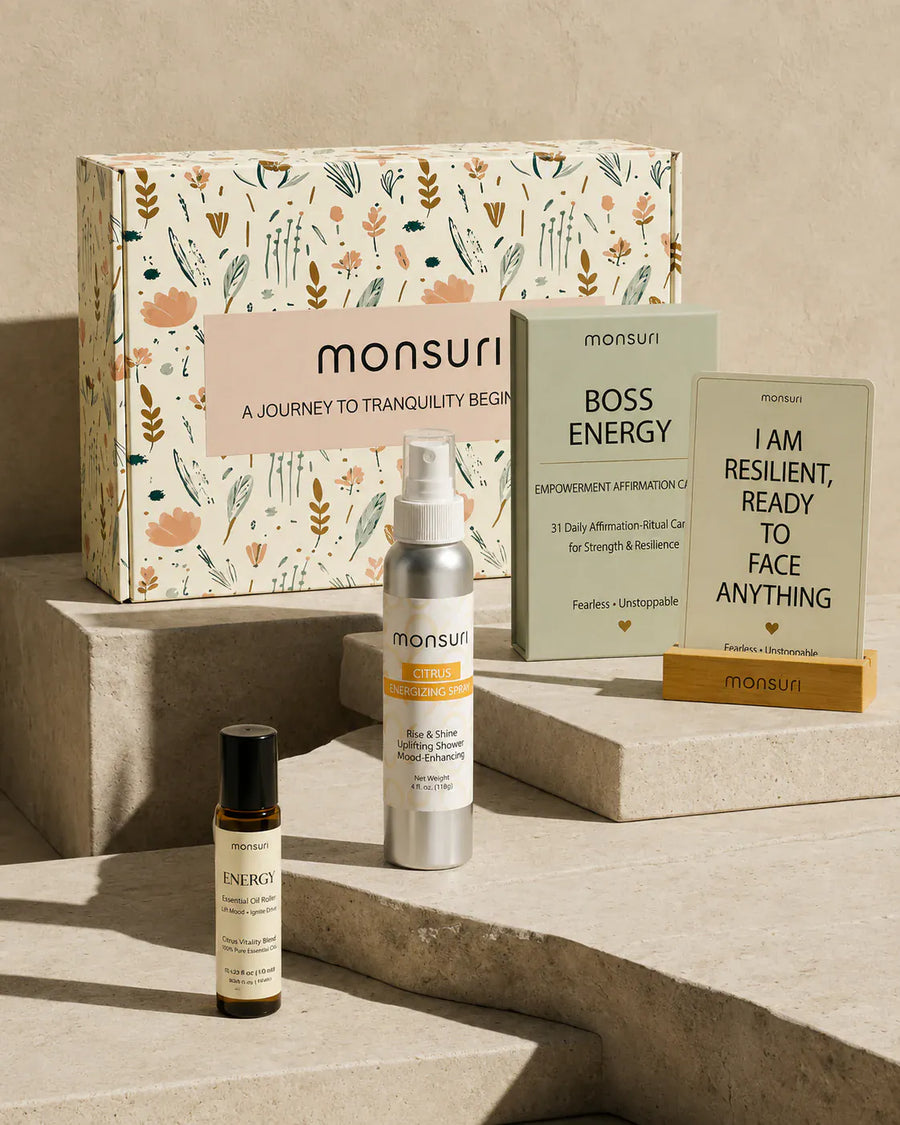 Confidence and Empowerment gift set on travertine steps in front of the Monsuri botanical gift box - BOSS ENERGY deck of 31 empowerment affirmation-ritual cards, a card reading I AM RESILIENT READY TO FACE ANYTHING in its wooden stand, the 4 fl oz citrus energizing shower spray and the ENERGY essential oil roller