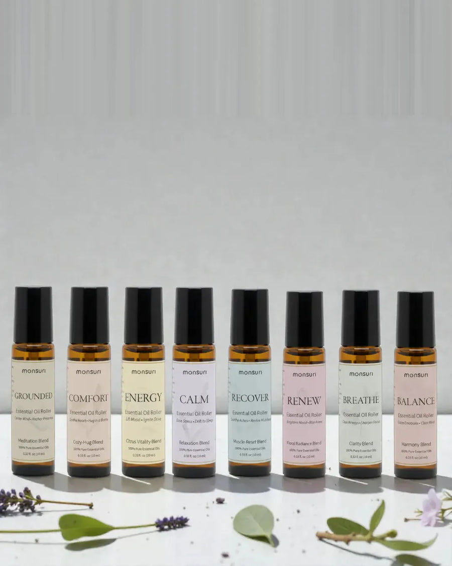 All eight Monsuri essential oil rollers standing in a row - GROUNDED meditation, COMFORT cozy-hug, ENERGY citrus vitality, CALM relaxation, RECOVER muscle-reset, RENEW floral radiance, BREATHE clarity and BALANCE harmony, 0.33 fl oz each, with lavender and eucalyptus