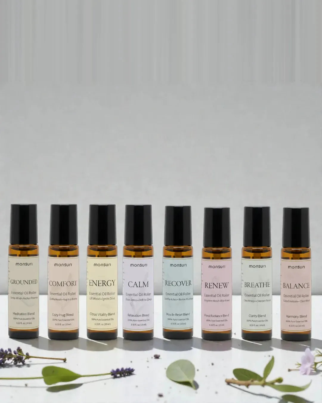 All eight Monsuri essential oil rollers standing in a row - GROUNDED meditation, COMFORT cozy-hug, ENERGY citrus vitality, CALM relaxation, RECOVER muscle-reset, RENEW floral radiance, BREATHE clarity and BALANCE harmony, 0.33 fl oz each, with lavender and eucalyptus