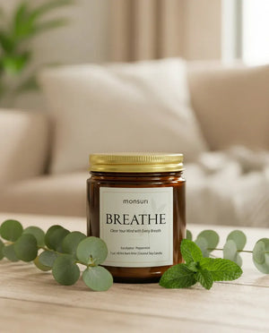 Monsuri BREATHE eucalyptus peppermint soy candle lit on a wood table with fresh eucalyptus sprigs and mint leaves, gold lid resting alongside.