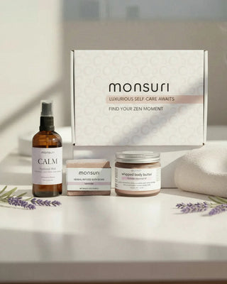 The Evening Wind Down bedtime trio in front of the Monsuri white gift box: the Calm Lavender Hydrosol Mist, the tranquil lavender bath bomb and the lavender whipped body butter, with dried lavender on a sunlit counter.