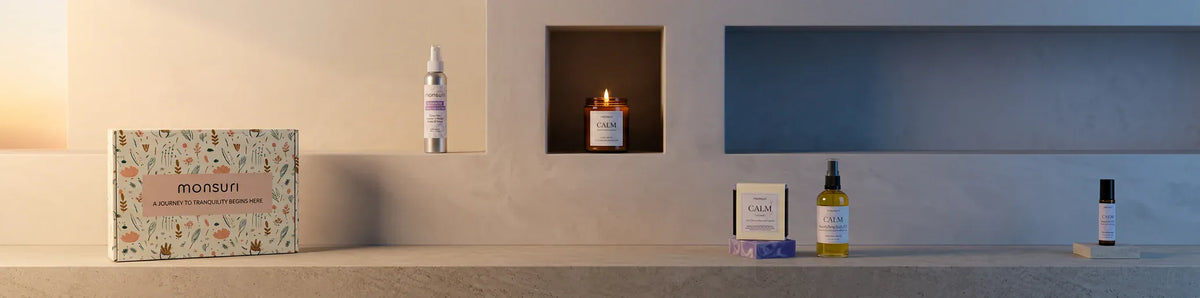 The Calm Moments Sanctuary set along a plaster ledge at dusk - the botanical gift box, the lavender shower spray, the lit CALM candle in an alcove, the lavender soap bar, the body oil and the essential oil roller