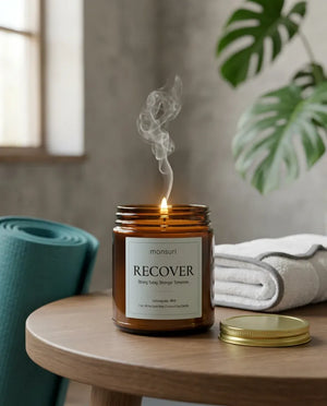 Monsuri RECOVER lemongrass mint candle burning on a side table next to a rolled teal yoga mat and folded towel, set up for a post-workout reset.