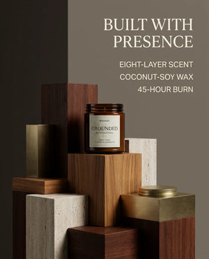 Monsuri GROUNDED candle benefits graphic listing eight-layer scent, coconut-soy wax, and 45-hour burn time, candle staged on stacked wood and stone blocks