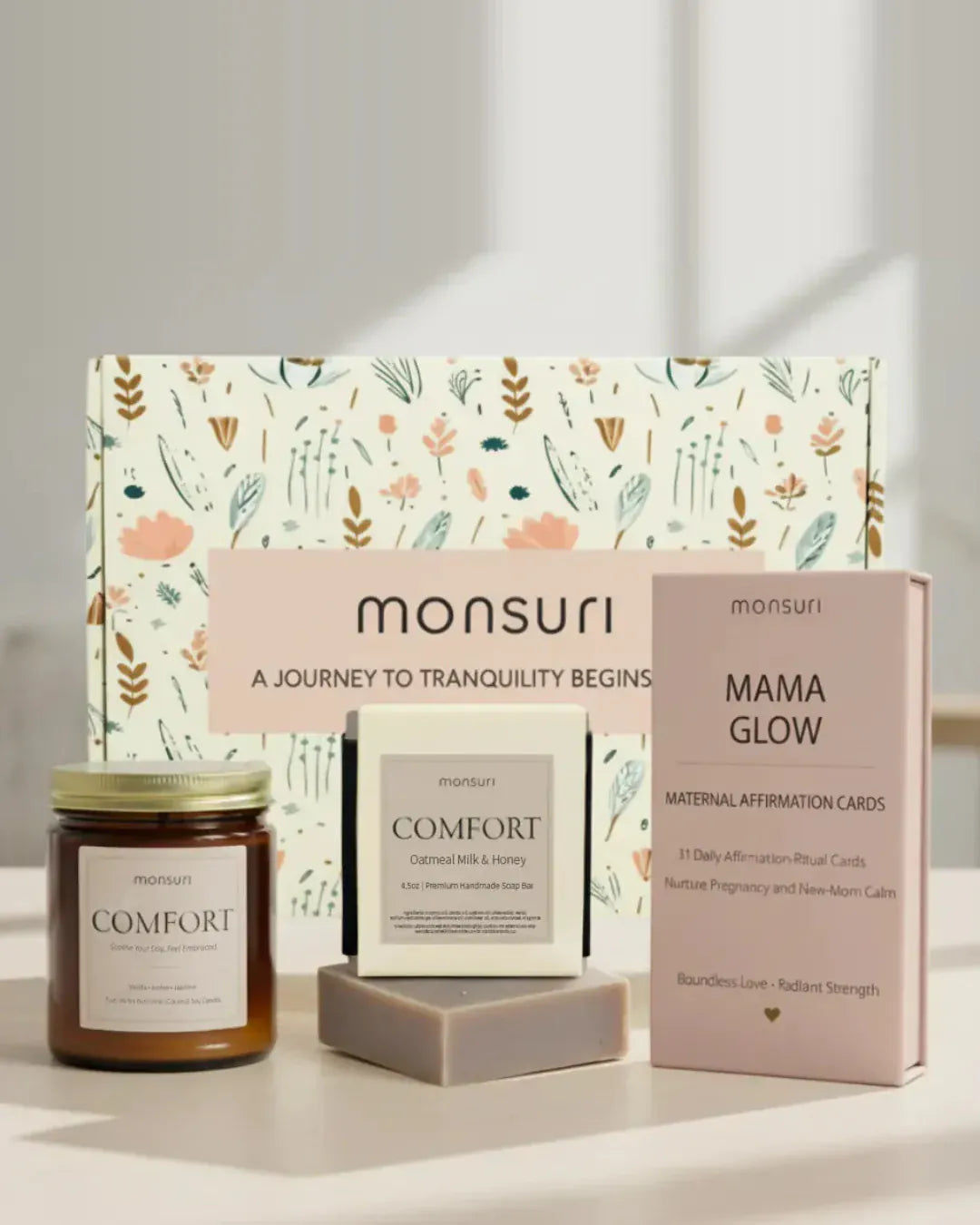 Mama Glow pregnancy and postpartum care set in front of the Monsuri botanical gift box - the COMFORT vanilla, amber and jasmine candle, the COMFORT oatmeal milk and honey soap bar, and the MAMA GLOW deck of 31 maternal affirmation-ritual cards
