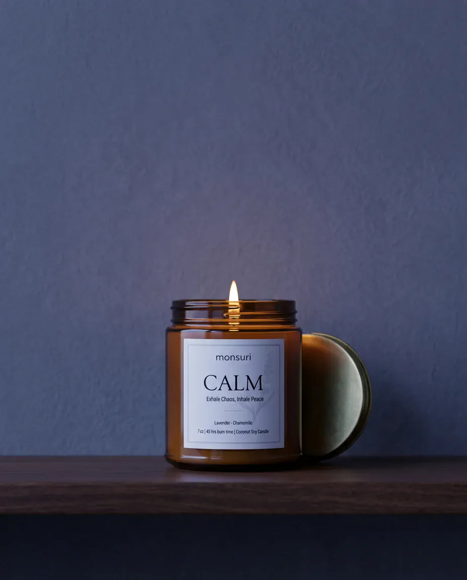 The CALM lavender and chamomile candle burning against a deep blue wall with its brass lid resting beside it