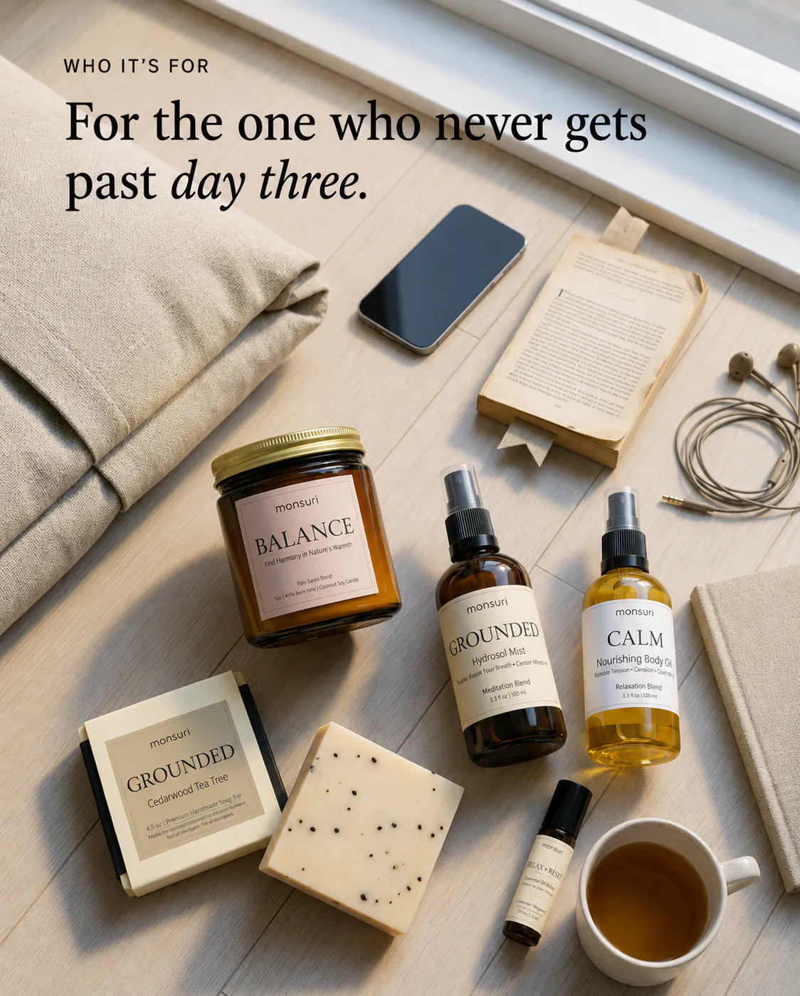 For the one who never gets past day three — the five pieces laid out overhead on pale floorboards beside a linen cushion, a phone face-up, an open paperback, earbuds and a cup of tea.