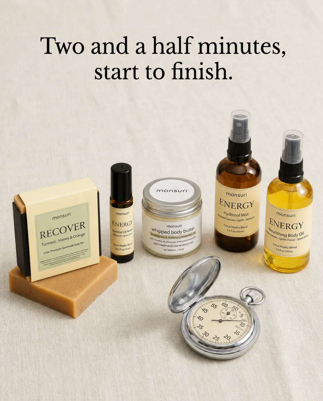 Two and a half minutes, start to finish: the whole five-piece energizing routine laid out on linen beside a stopwatch — the RECOVER turmeric soap, the energy roller, the lemongrass-rosemary body butter, the citrus hydrosol mist and the nourishing body oil.
