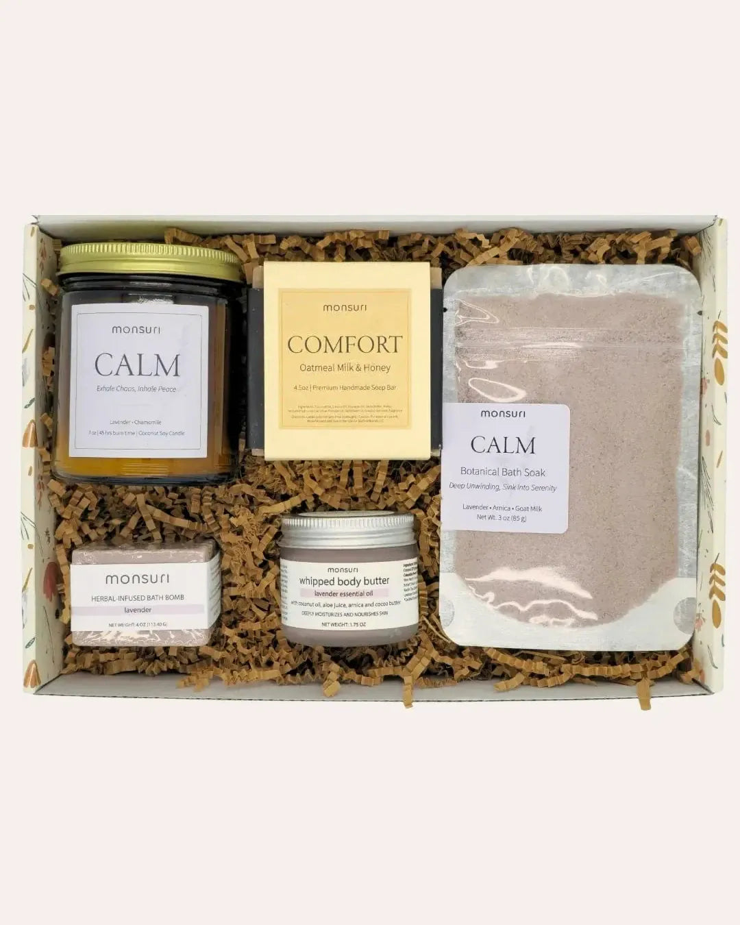 Mom's Wind-Down Ritual arranged inside its botanical kraft gift box on kraft shred, seen from above: the CALM lavender chamomile candle, the COMFORT oatmeal milk and honey soap bar, the CALM botanical bath soak pouch, the herbal-infused lavender bath bomb and the lavender whipped body butter.