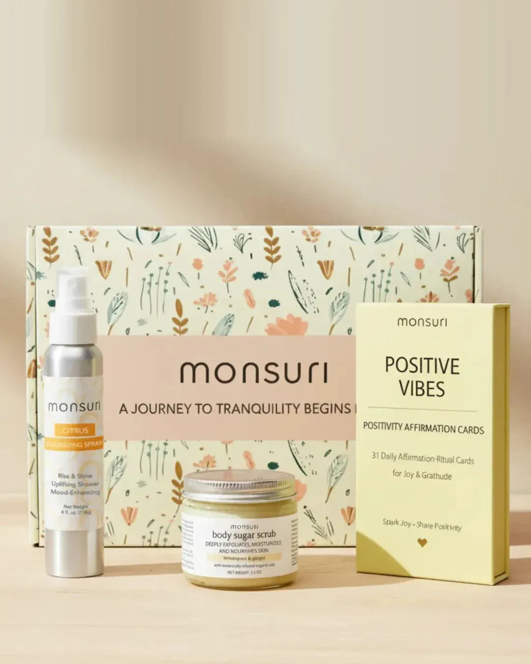Positivity Boost gift set in front of the Monsuri botanical gift box - 4 fl oz citrus energizing shower spray in brushed aluminium, 2.5 oz lemongrass and ginger body sugar scrub and the POSITIVE VIBES deck of 31 daily affirmation-ritual cards