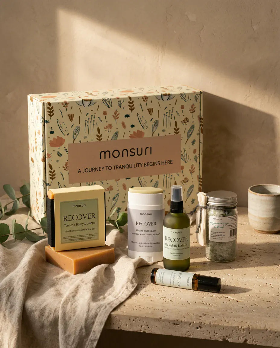 The Monsuri botanical kraft gift box standing behind all five recovery pieces on a travertine ledge, printed "A journey to tranquility begins here", with a linen cloth and a eucalyptus sprig at the edge.