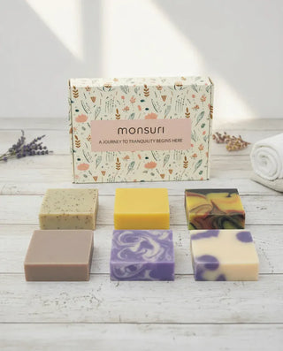 Monsuri Rest & Renewal soap gift set — six full-size handmade bars and the botanical gift box laid out on white wood.