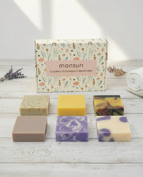 Monsuri Rest & Renewal soap gift set — six full-size handmade bars and the botanical gift box laid out on white wood.