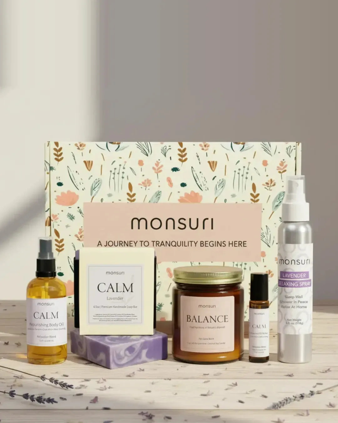 All five pieces of the Retirement Relaxation gift set in front of the botanical gift box - CALM nourishing body oil, CALM lavender handmade soap, BALANCE palo santo candle, CALM essential oil roller and the lavender relaxing spray on pale wood with dried lavender