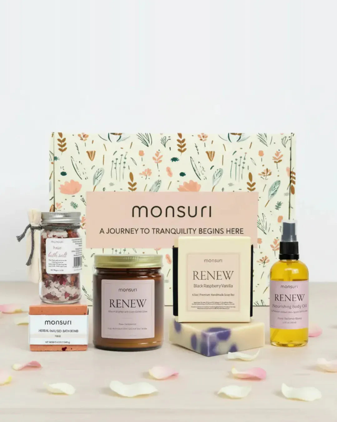 Romantic spa gift set arranged in front of the Monsuri botanical kraft gift box - rose bath salt jar 1.5 oz, herbal-infused rose bath bomb 4 oz, RENEW rose and sandalwood candle 7 oz, black raspberry vanilla soap bar 4.5 oz and nourishing body oil 3.3 fl oz, scattered with fresh rose petals