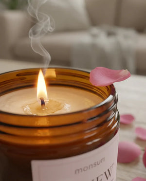 Close-up of the Monsuri RENEW rose sandalwood candle's lit wick and melted wax pool, with a single pink rose petal resting on the jar rim.
