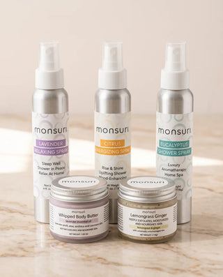 All five pieces of the Monsuri Sensory Symphony set on a marble counter - the lavender, citrus and eucalyptus 4 oz shower sprays behind the whipped body butter and the lemongrass ginger sugar scrub