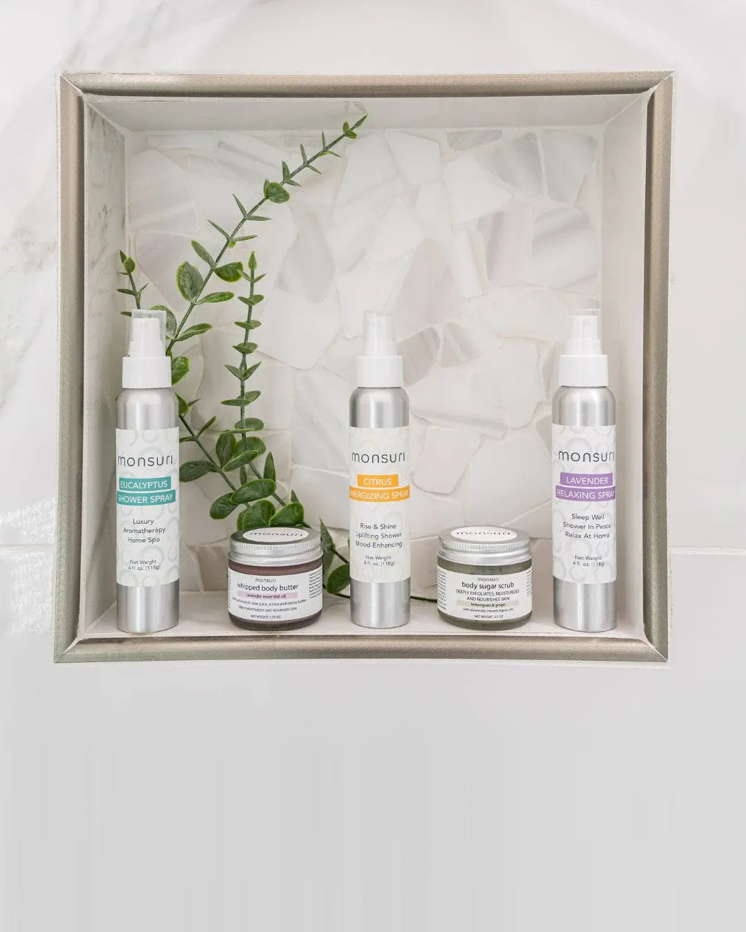 The Monsuri Sensory Symphony gift set presented in a white display box - the eucalyptus, citrus and lavender 4 oz shower sprays standing behind the whipped body butter and lemongrass ginger sugar scrub jars, with a eucalyptus sprig