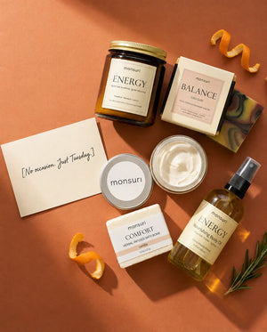 Overhead on terracotta: the five pieces around a handwritten card reading "No occasion. Just Tuesday.", with the body butter open, curls of orange peel and a sprig of rosemary.