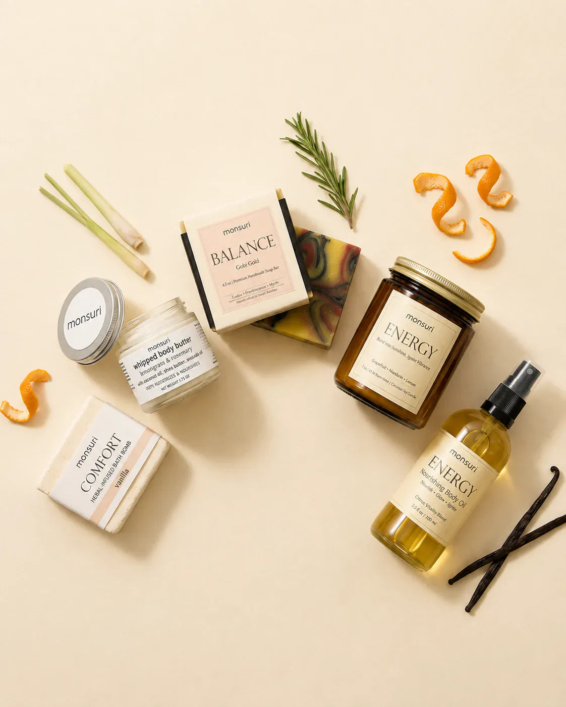 Overhead flat lay of the five pieces on cream with their ingredients scattered between them — lemongrass stalks, rosemary, curls of orange peel and vanilla pods.