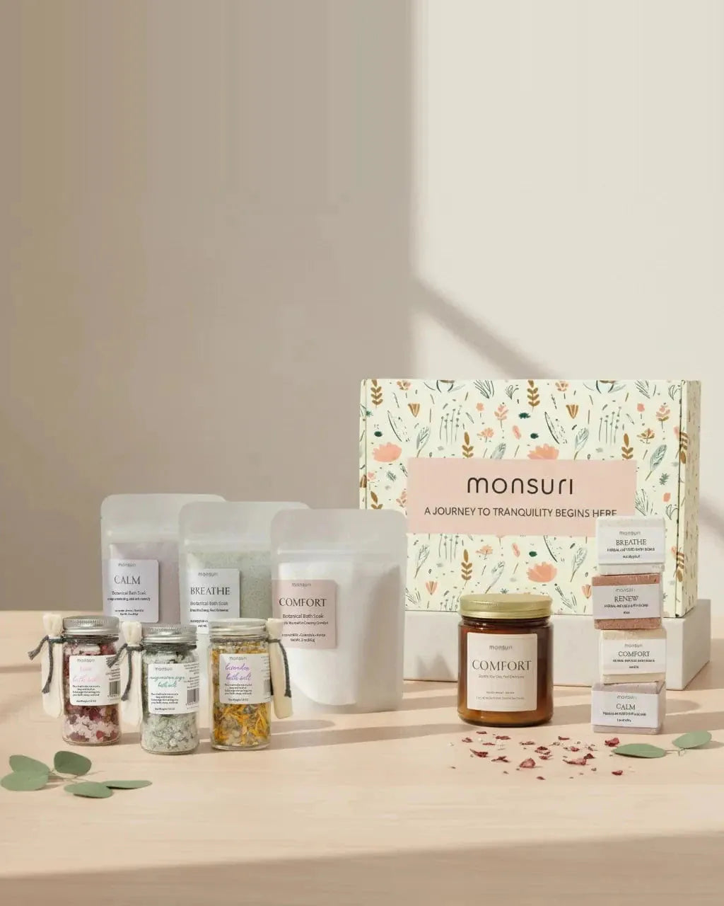 The eleven pieces of the Ultimate Bath Gift Set arranged in front of the Monsuri botanical gift box they arrive in, on a pale wood table