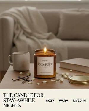 Infographic reading 'The Candle for Stay-Awhile Nights' with a lit Monsuri COMFORT candle on a coffee table beside a mug and book, tagged cozy, warm, lived-in.