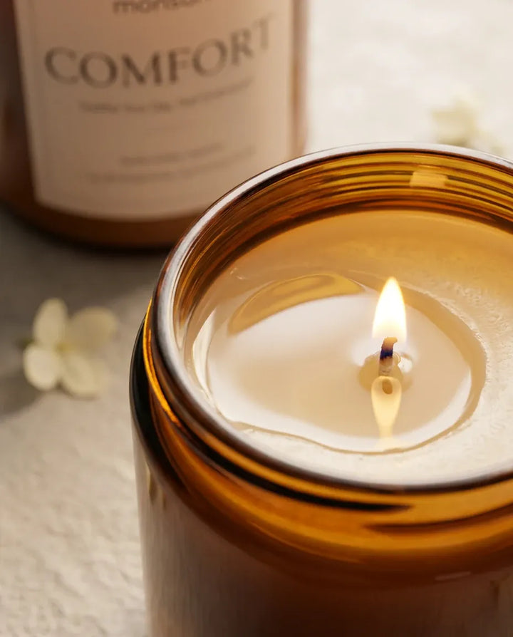 Close-up of the lit wick and clean wax pool on a Monsuri COMFORT vanilla amber candle, showing the coconut-soy wax burning evenly to the glass edge.