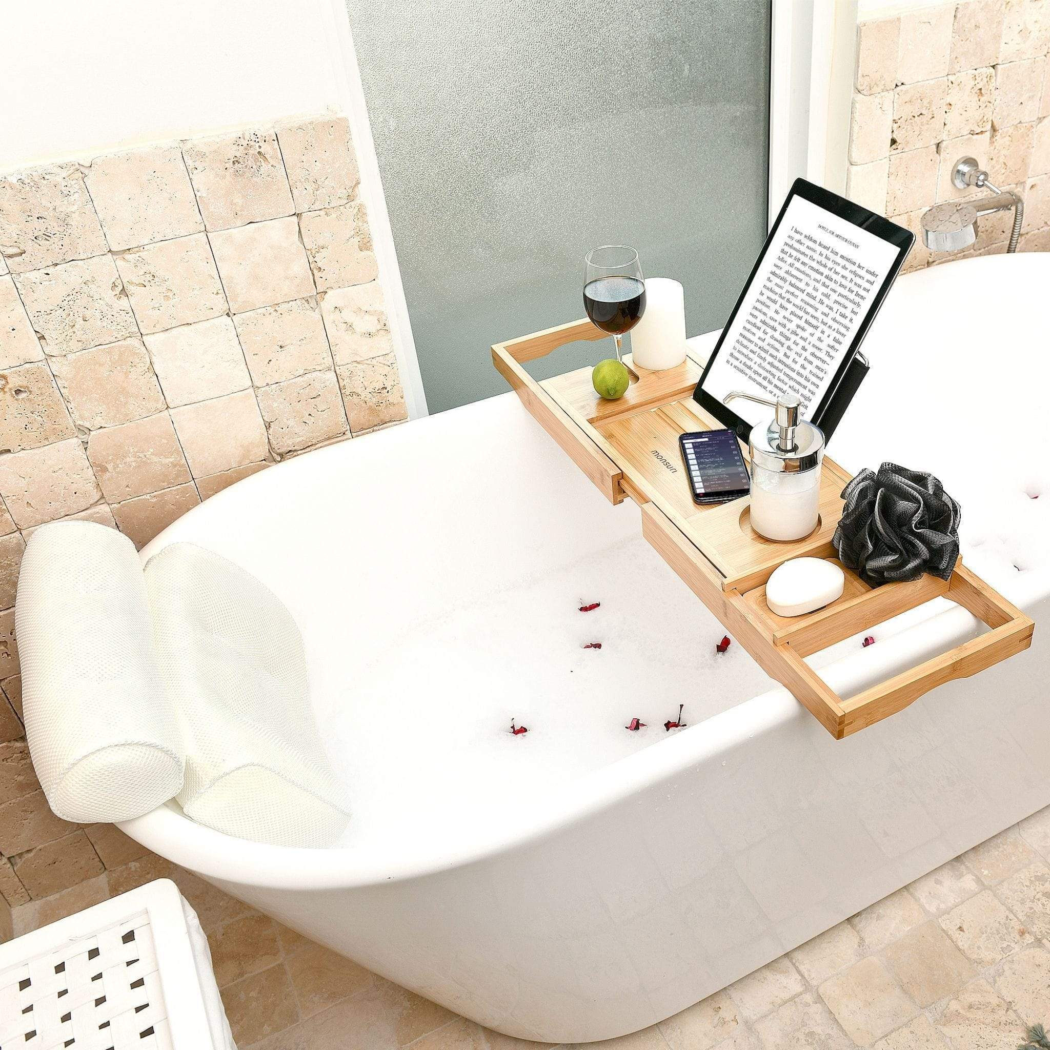 Self-care Sunday bath setup — the Monsuri bath tray and pillow set bridging a tub with candle, book, body oil bottle, and water within reach; the structural pair that makes a 20-minute Sunday soak physically possible without the neck giving up